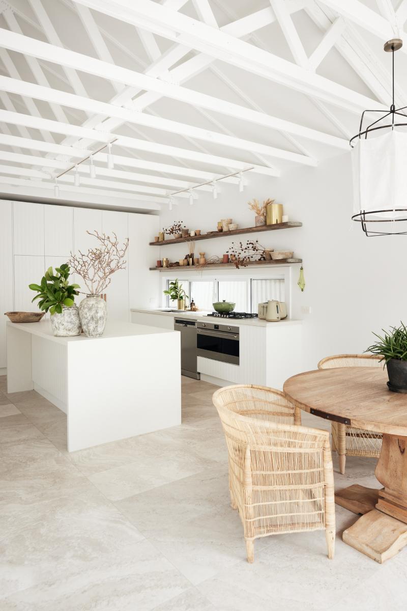Modern open-plan kitchen with white cabinetry, exposed beam ceiling, and wooden dining area
